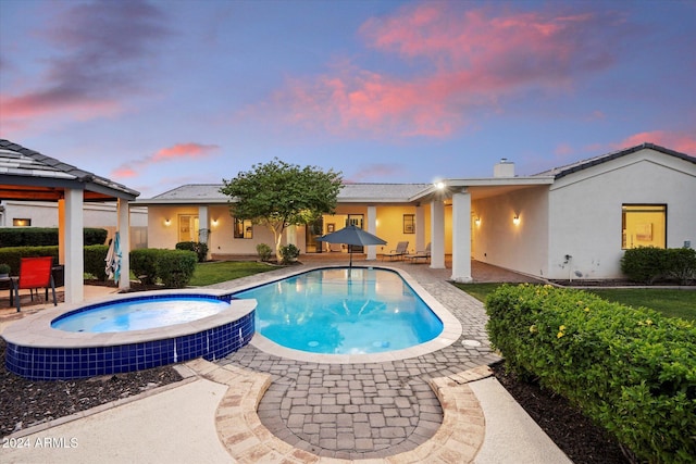 pool at dusk featuring an in ground hot tub and a patio area