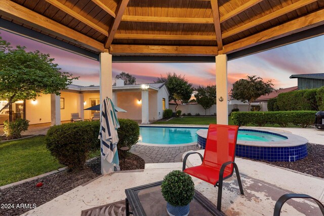 pool at dusk with a gazebo and an in ground hot tub