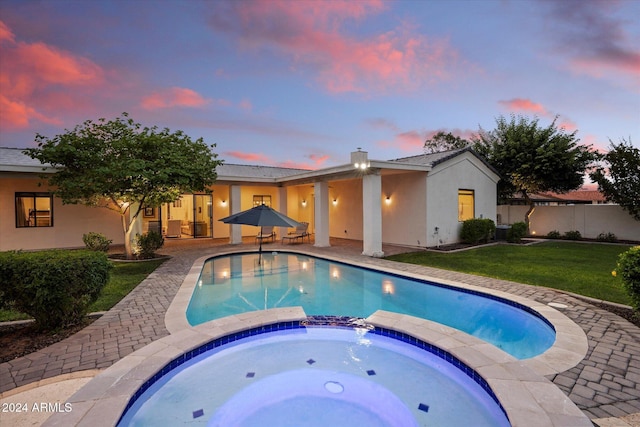 pool at dusk with an in ground hot tub, a patio area, and a lawn