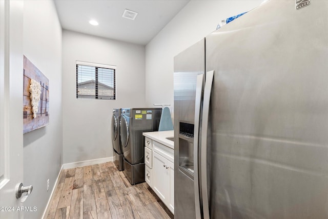 laundry room featuring washer and dryer, light hardwood / wood-style flooring, and cabinets