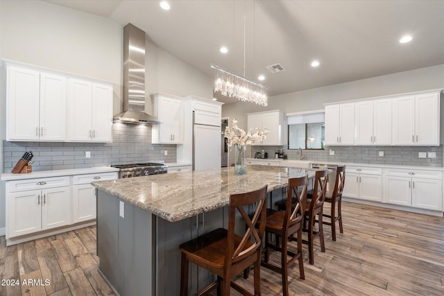 kitchen with a center island, white cabinets, paneled built in fridge, hardwood / wood-style flooring, and wall chimney exhaust hood