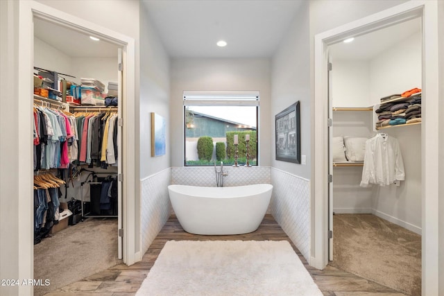 bathroom with wood-type flooring, a tub to relax in, and tile walls