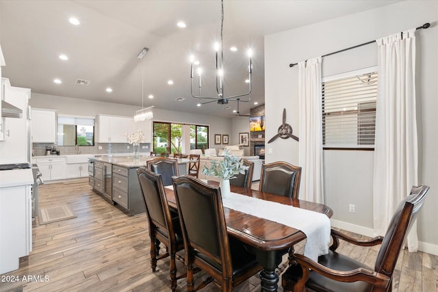 dining area featuring light hardwood / wood-style floors, a fireplace, wine cooler, and an inviting chandelier