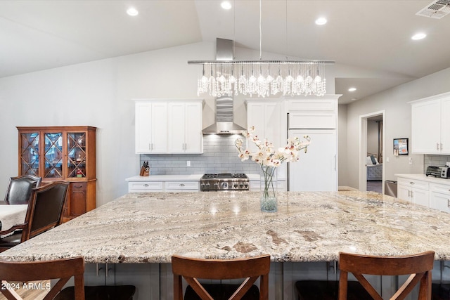 kitchen with white cabinets, vaulted ceiling, wall chimney exhaust hood, a large island, and a breakfast bar area