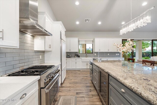 kitchen featuring white cabinets, light wood-type flooring, high end stainless steel range oven, and wall chimney exhaust hood