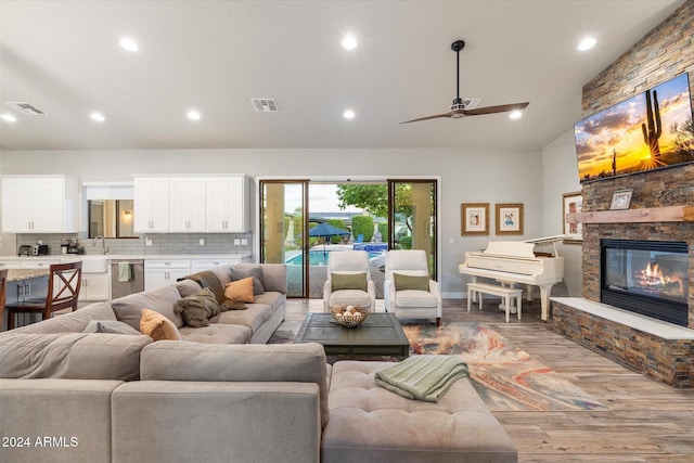 living room featuring a stone fireplace, ceiling fan, sink, and light wood-type flooring