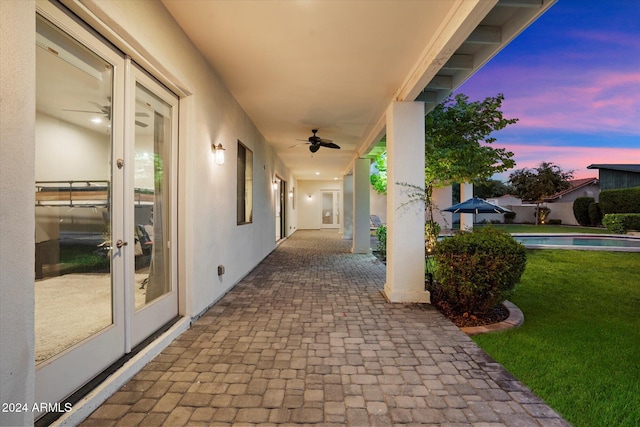 patio terrace at dusk with french doors, a yard, and ceiling fan