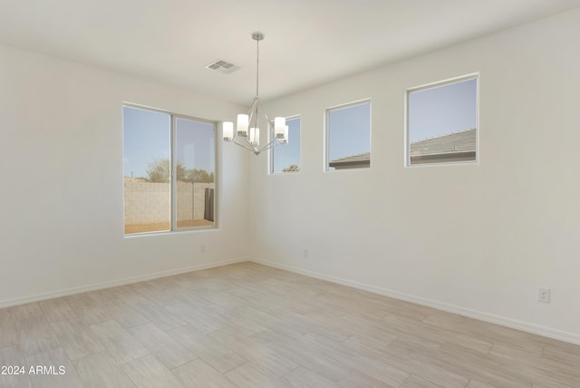 empty room featuring light wood-type flooring, visible vents, baseboards, and an inviting chandelier