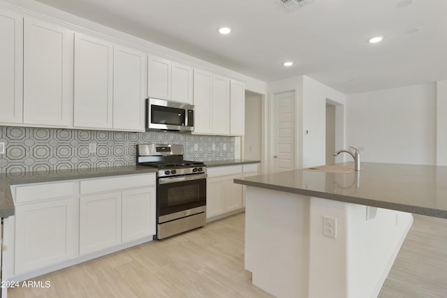 kitchen featuring tasteful backsplash, white cabinets, a sink, light wood-style floors, and stainless steel appliances