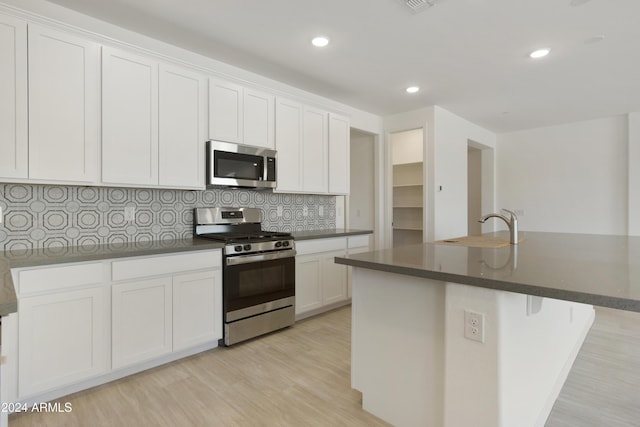 kitchen with stainless steel appliances, light wood-style flooring, a sink, and decorative backsplash