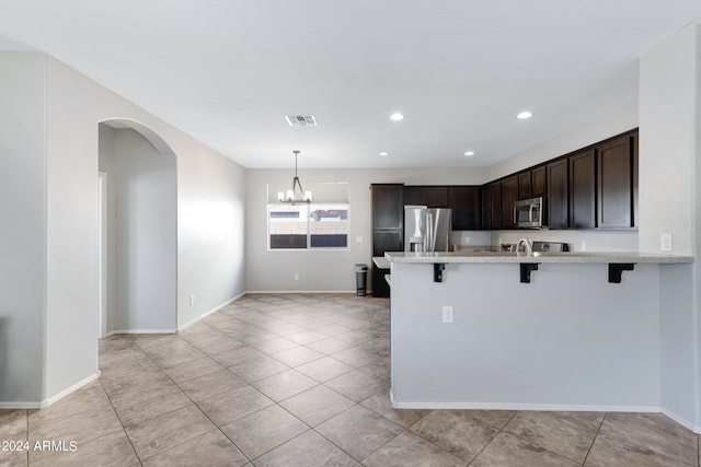 kitchen featuring dark brown cabinets, a chandelier, a kitchen bar, hanging light fixtures, and stainless steel appliances