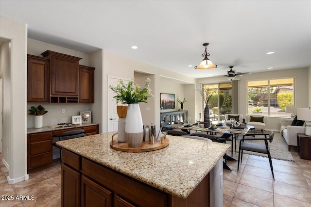 kitchen with light stone counters, ceiling fan, a center island, hanging light fixtures, and light tile patterned flooring