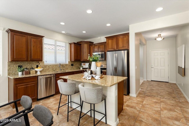 kitchen featuring sink, decorative backsplash, a kitchen island, light stone counters, and stainless steel appliances