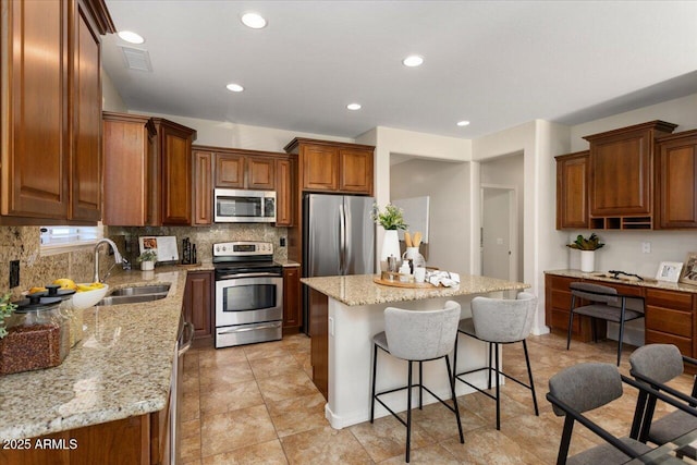 kitchen featuring tasteful backsplash, light stone counters, stainless steel appliances, sink, and a center island