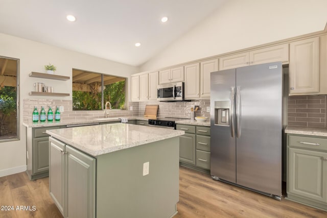 kitchen featuring a center island, vaulted ceiling, light wood-type flooring, appliances with stainless steel finishes, and tasteful backsplash