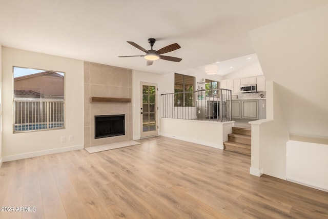 unfurnished living room with ceiling fan, light wood-type flooring, a tile fireplace, and lofted ceiling