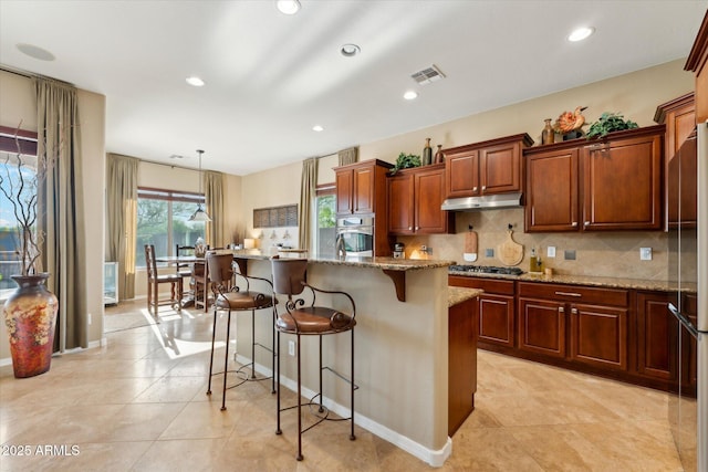 27308 N 56th Dr, Phoenix, AZ 85083 - kitchen featuring appliances with stainless steel finishes, under cabinet range hood, a kitchen bar, backsplash, and light stone countertops
