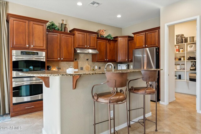 27308 N 56th Dr, Phoenix, AZ 85083 - kitchen featuring appliances with stainless steel finishes, under cabinet range hood, a kitchen breakfast bar, backsplash, and light stone countertops