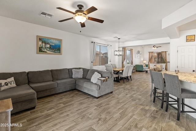 living room featuring visible vents, light wood finished floors, and ceiling fan with notable chandelier