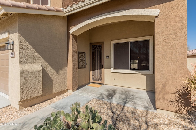 doorway to property featuring a garage, a tile roof, and stucco siding