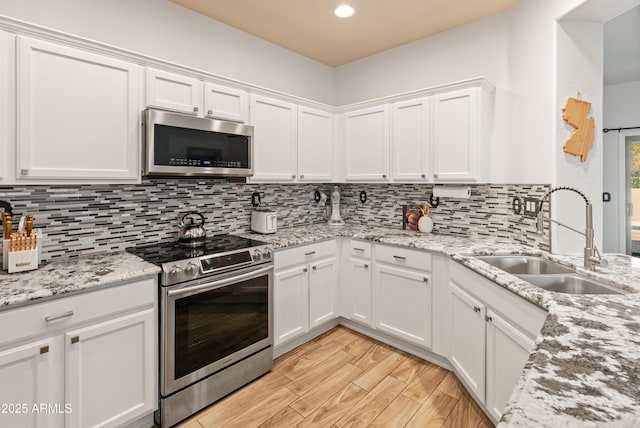 kitchen with appliances with stainless steel finishes, white cabinetry, a sink, and light wood-style flooring