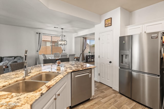 kitchen featuring light stone counters, stainless steel appliances, light wood-style floors, white cabinetry, and a sink