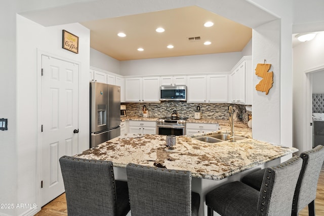 kitchen featuring tasteful backsplash, visible vents, appliances with stainless steel finishes, a sink, and a peninsula