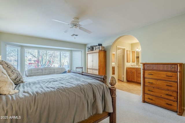 bedroom with ceiling fan, ensuite bathroom, and light carpet