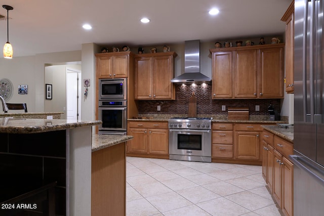 kitchen featuring wall chimney exhaust hood, hanging light fixtures, appliances with stainless steel finishes, dark stone counters, and decorative backsplash