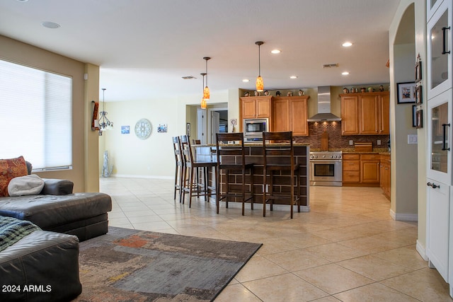 kitchen with wall chimney exhaust hood, a kitchen bar, tasteful backsplash, light tile patterned floors, and stainless steel appliances