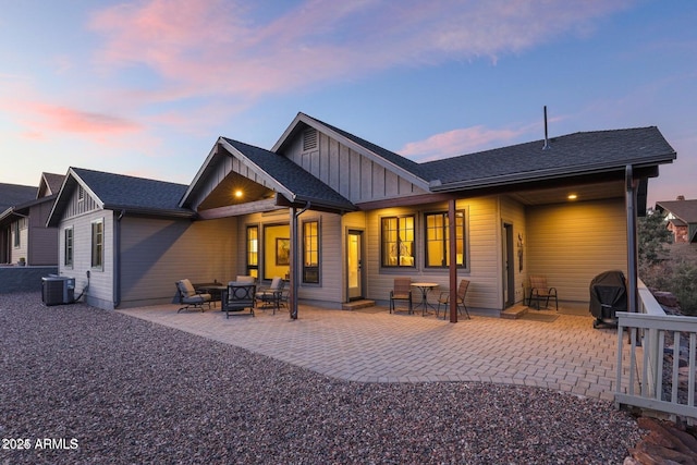 back house at dusk with ceiling fan, central AC unit, and a patio