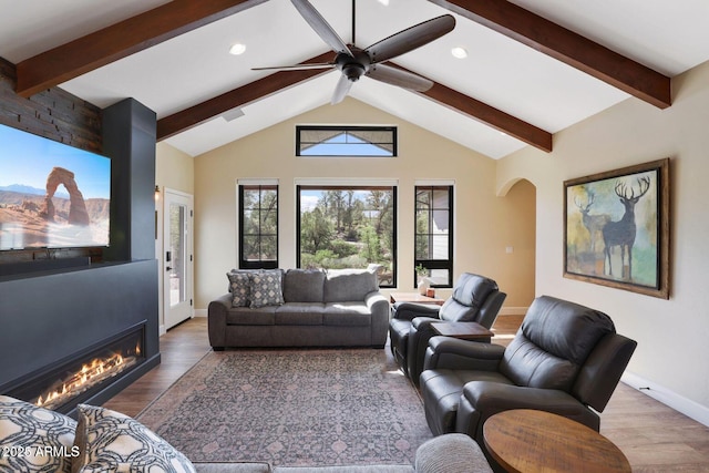 living room with ceiling fan, a large fireplace, dark hardwood / wood-style flooring, and vaulted ceiling with beams