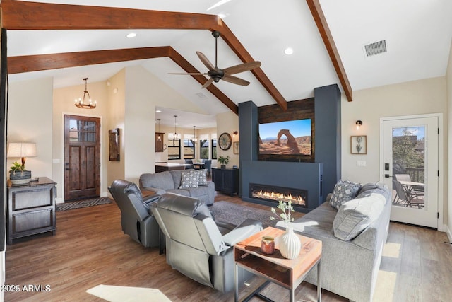 living room featuring wood-type flooring, a fireplace, ceiling fan with notable chandelier, and vaulted ceiling with beams