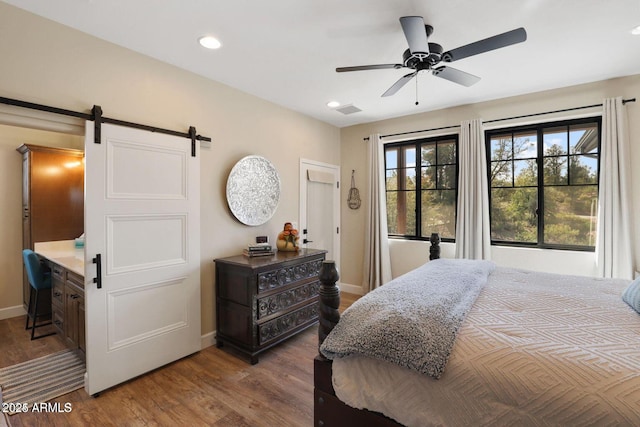 bedroom featuring a barn door, dark hardwood / wood-style floors, and ceiling fan