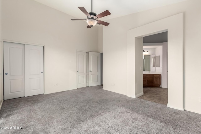 unfurnished bedroom featuring carpet, ceiling fan, connected bathroom, and two closets