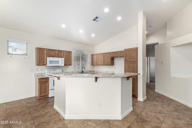 kitchen with light stone countertops, sink, white appliances, a breakfast bar, and a center island with sink