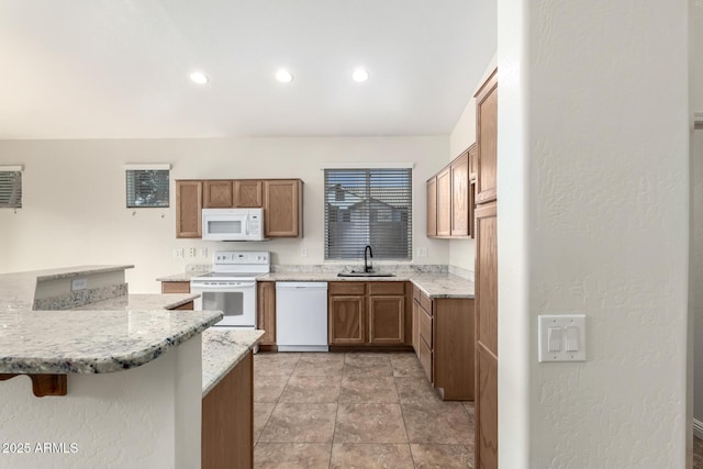 kitchen with white appliances, sink, light stone countertops, kitchen peninsula, and a breakfast bar area