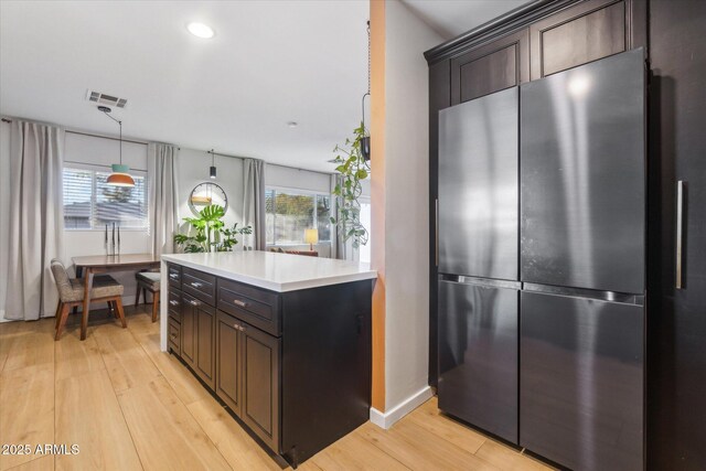 kitchen with dark brown cabinetry, light hardwood / wood-style floors, and stainless steel fridge