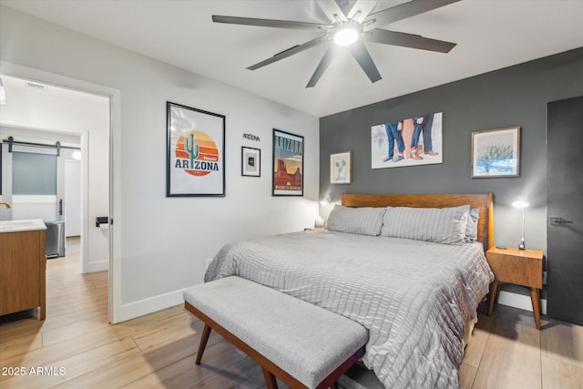 bedroom with ceiling fan, light hardwood / wood-style flooring, and a barn door