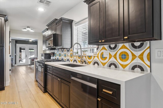 kitchen featuring sink, range with gas cooktop, black dishwasher, light hardwood / wood-style flooring, and decorative backsplash