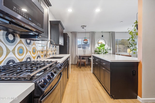 kitchen featuring gas stove, decorative backsplash, dark brown cabinetry, sink, and light hardwood / wood-style flooring