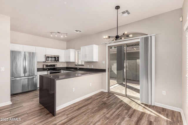 kitchen with appliances with stainless steel finishes, white cabinetry, hardwood / wood-style floors, a healthy amount of sunlight, and kitchen peninsula