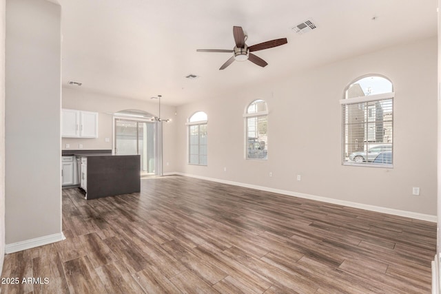 unfurnished living room with dark wood-type flooring and ceiling fan with notable chandelier