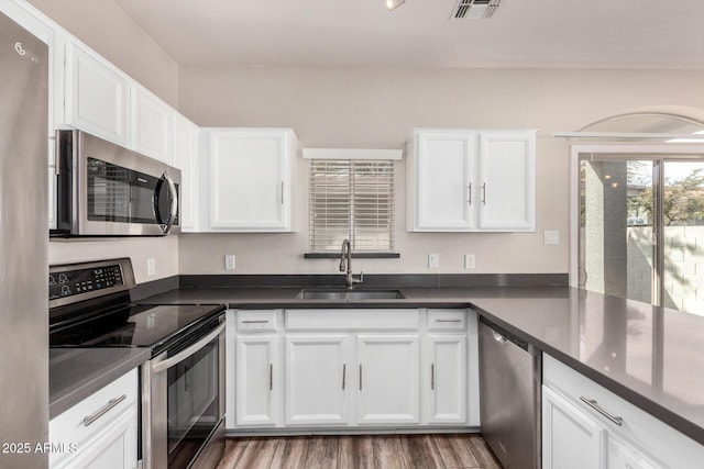 kitchen with appliances with stainless steel finishes, sink, hardwood / wood-style floors, and white cabinets