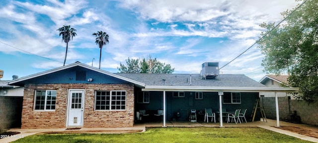 back of house with roof with shingles, a patio, a lawn, cooling unit, and stone siding