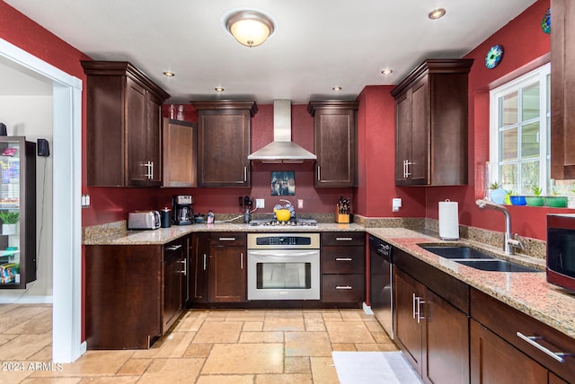 kitchen featuring light stone counters, stone tile floors, stainless steel appliances, a sink, and wall chimney range hood