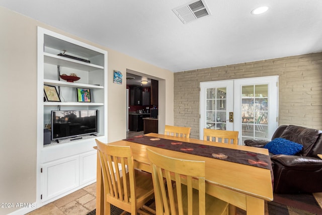 dining area with built in features, french doors, visible vents, stone finish floor, and brick wall