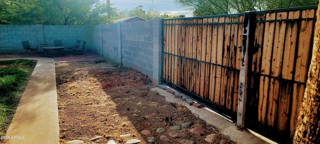 view of gate with a patio area, a fenced backyard, and a fire pit