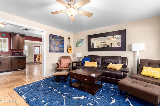 living room featuring visible vents, baseboards, a ceiling fan, and stone tile floors