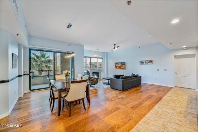 dining space with light wood-type flooring, a tiled fireplace, and ceiling fan